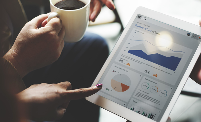 person drinking coffee and looking at business charts on a tablet