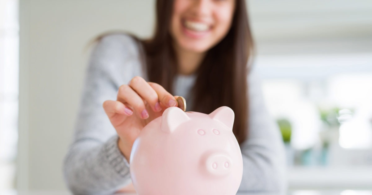 Young woman inserting coin into pink piggy bank