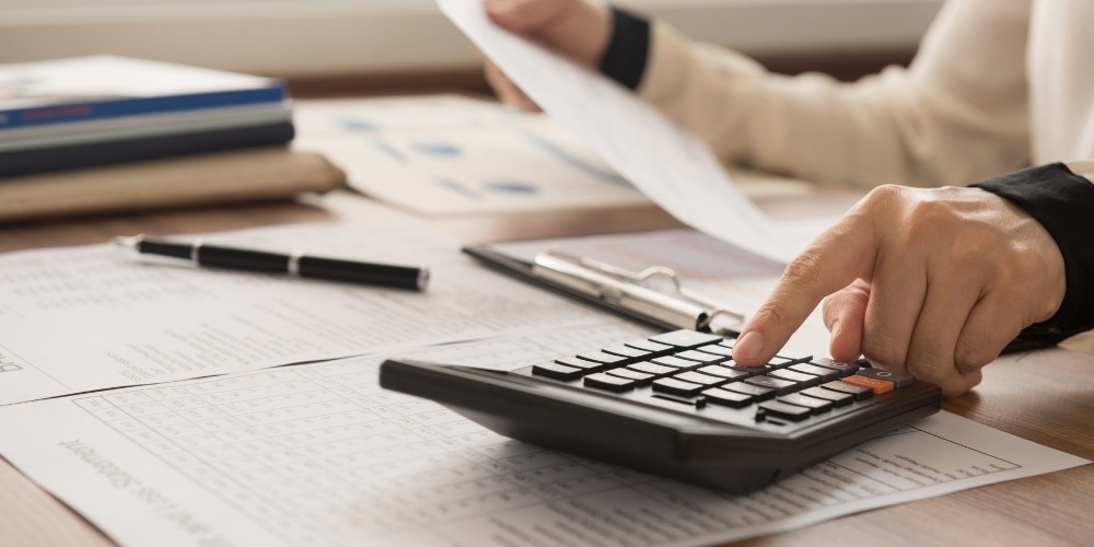 using a black calculator on a desk filled with paper documents
