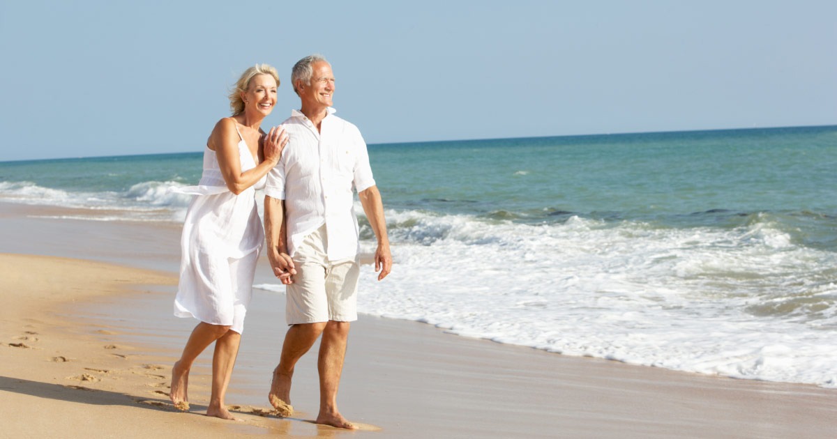 Older couple walking along the ocean on the beach sand
