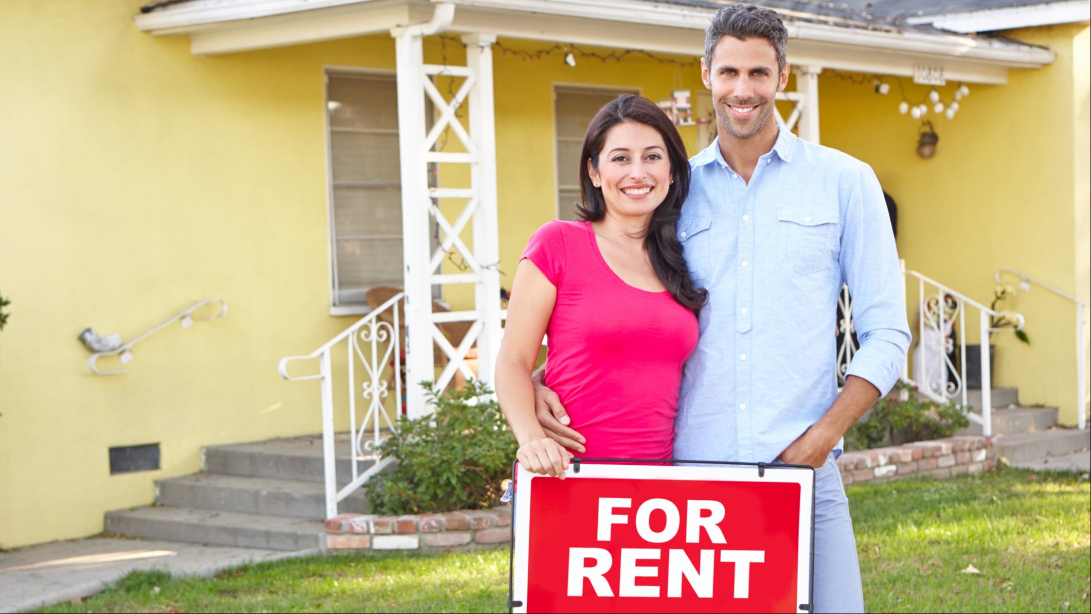 Photo image of couple holding a for rent sign in front of yellow house