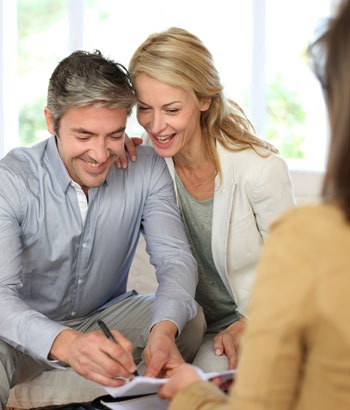 Woman holding man's shoulder while he writes on paper