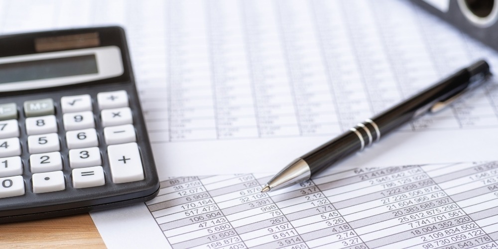 desktop calculator, a sleek silver and black pen, and financial spreadsheets