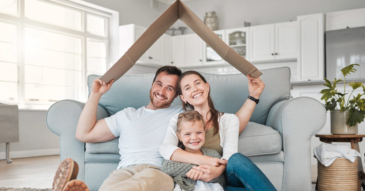Husband holding roof-shaped cardboard box over his wife and daughter