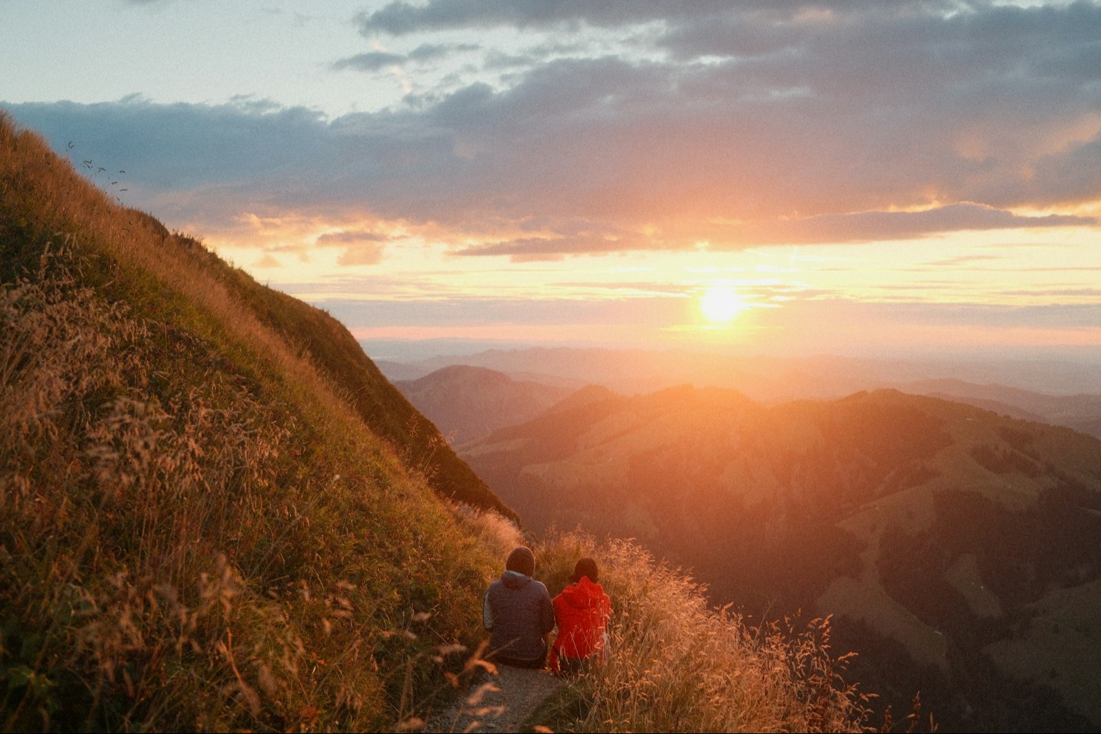 Couple resting together on a mountain trail at sunset