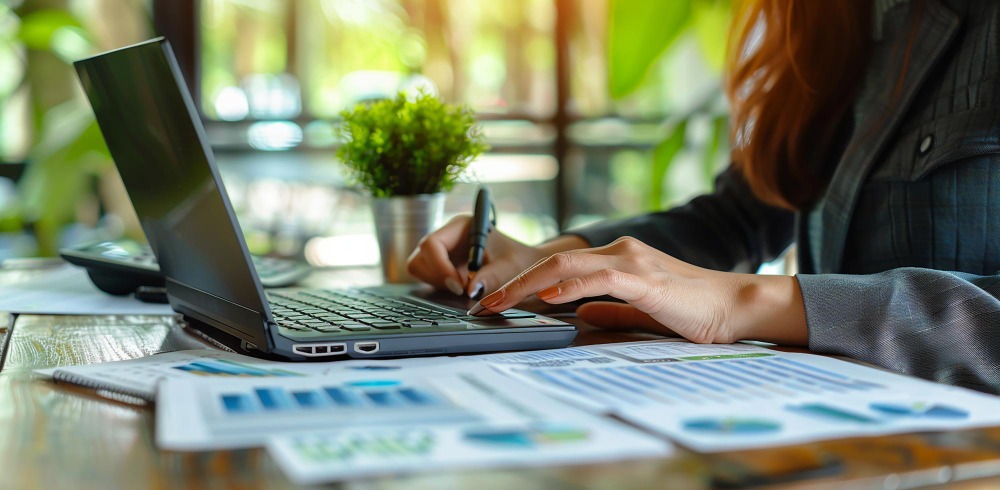 Entrepreneur conducting a business audit and tracking key performance indicators on a laptop surrounded by charts and office plants.