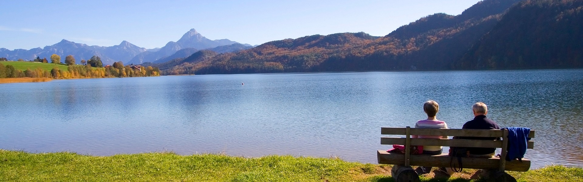couple sitting on a bench next to a lake with mountains in the distance