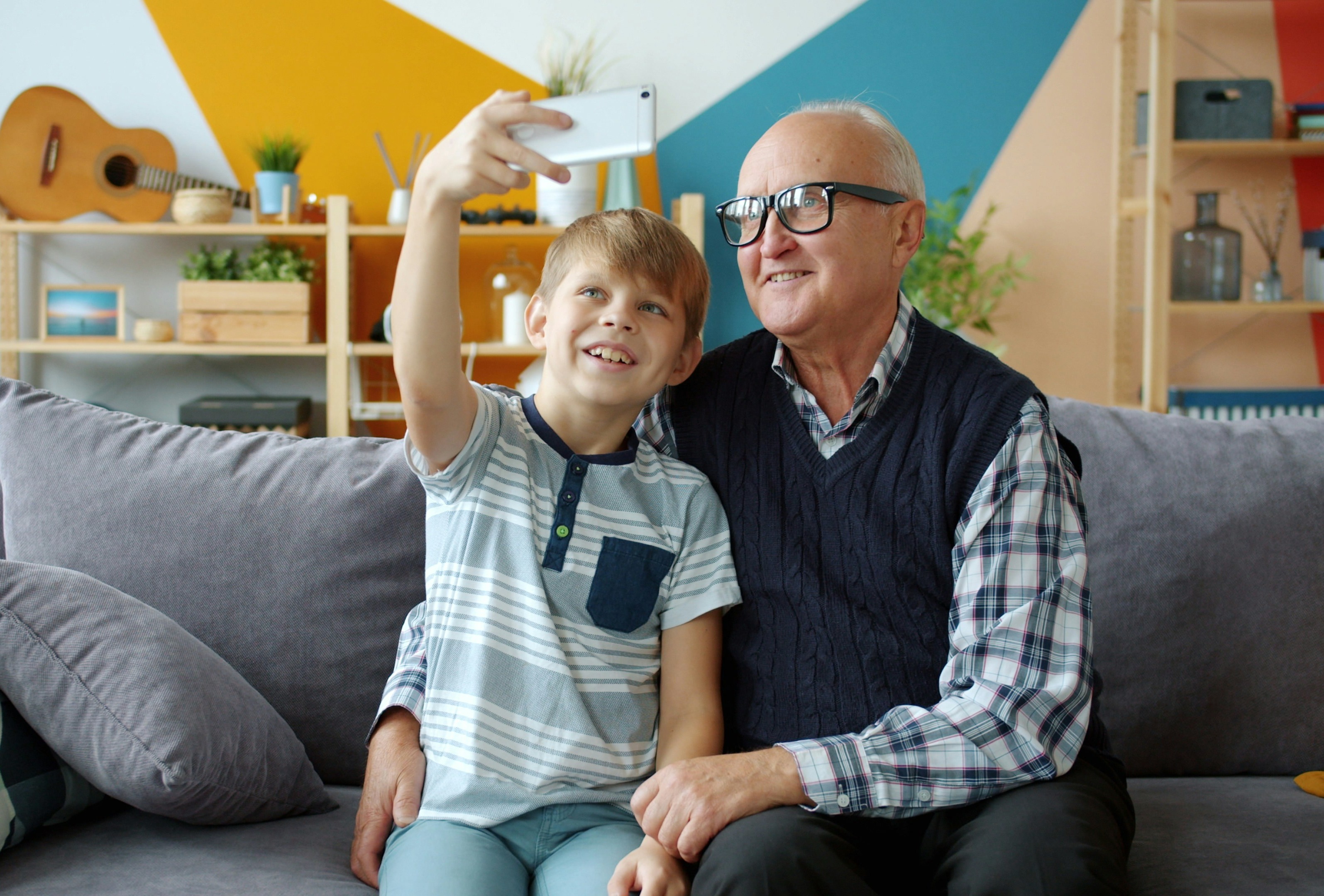 A grandfather and grandson smiling and taking a photo together on the couch