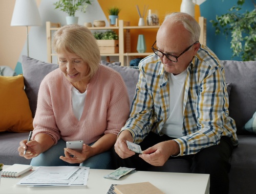 An older couple reviewing their finances together on the couch with paperwork and a phone, during pre-retirement planning.