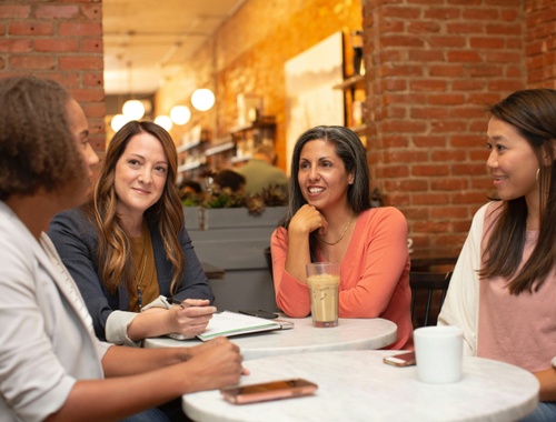 Four professional women talking together around a cafe table, meeting with a financial advisor for women.