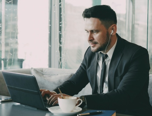 A business owner in a suit working on a laptop with earbuds and a coffee, illustrating financial planning for small business owners.