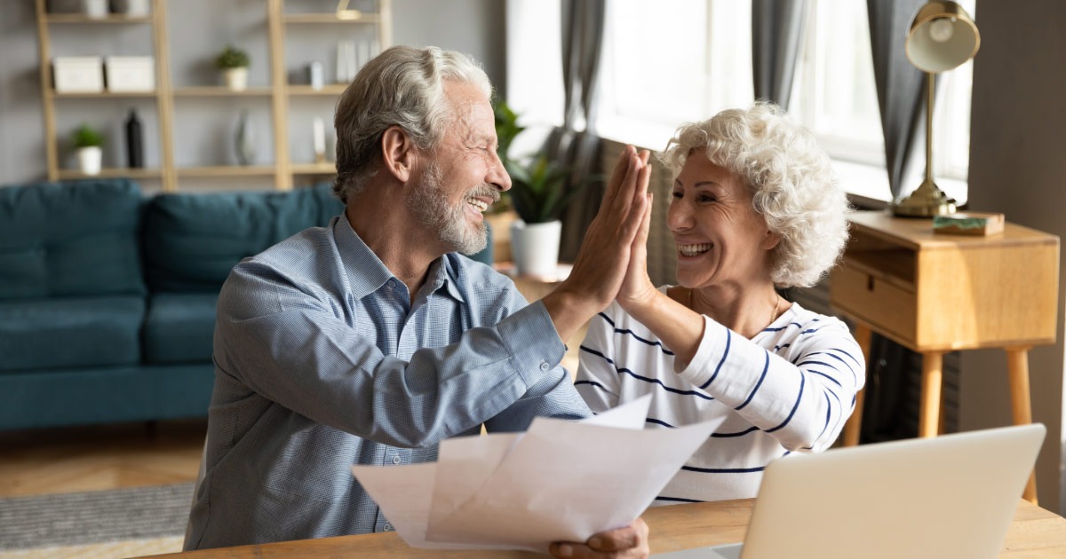 Older couple high-fiving while reviewing their financial status