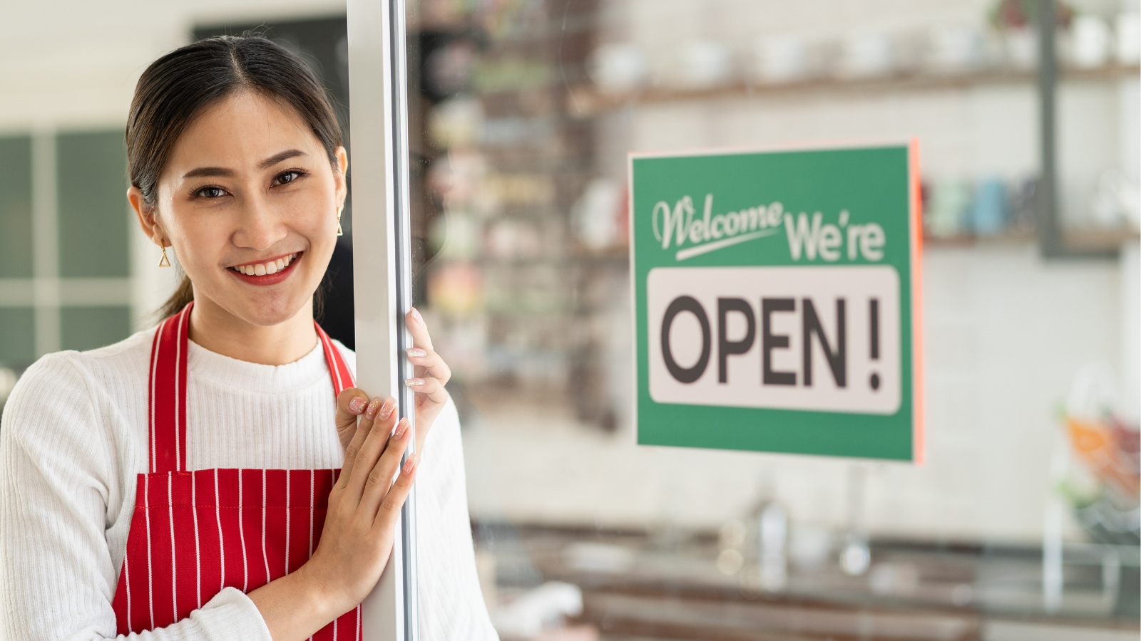 Photo of a young woman standing in front of a store front; appears to be the owner