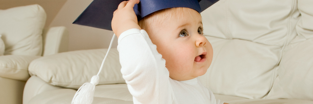 toddler holding on to a couch wearing a graduation cap