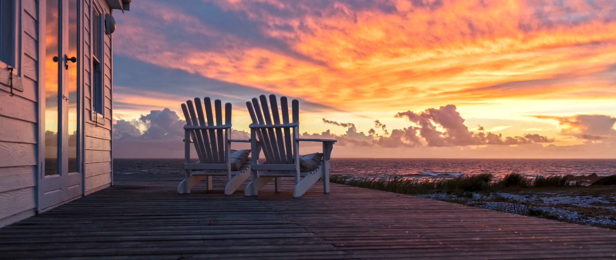 2 empty Adirondack chairs on a deck facing the sunset. 