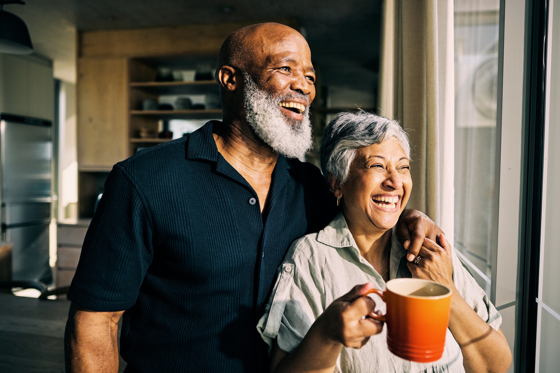 A smiling couple looking out a sunlit window together