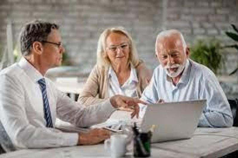 Man with tie pointing at laptop while elderly man and woman look at it