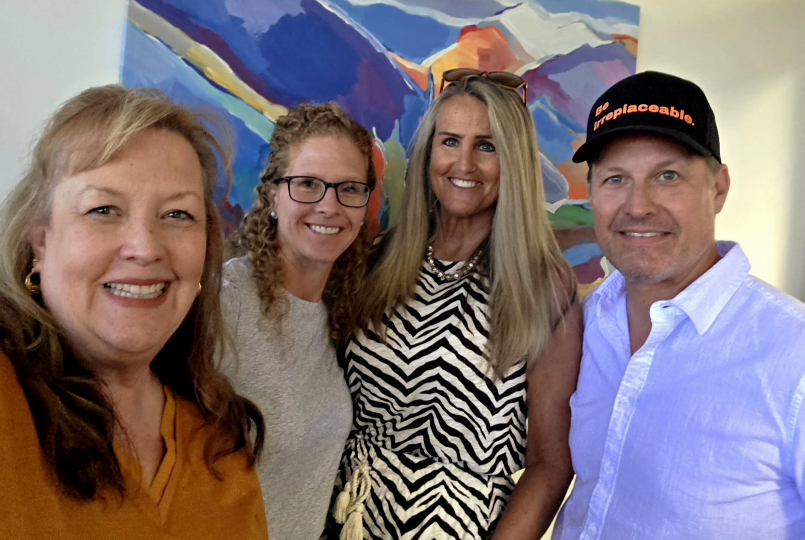 Four members of the SWP team smiling in front of a colorful abstract mountain painting