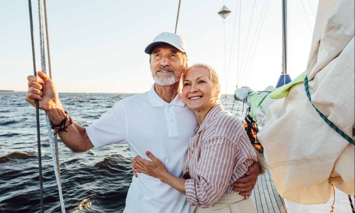 Older gentleman and his wife enjoying retirement after moving their 401K in Canada, sailing happily on a luxurious sailboat.