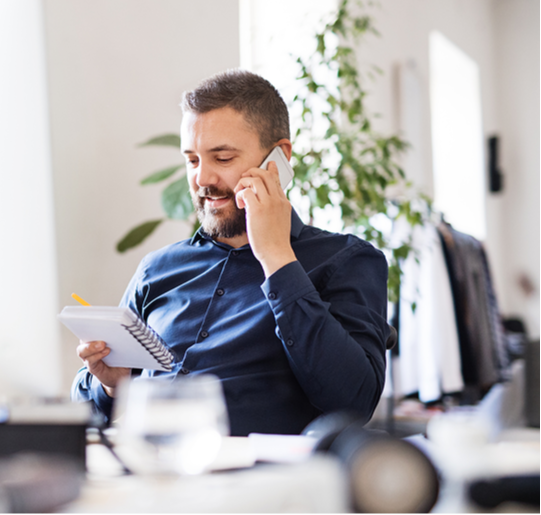 man looks over notepad while on the phone