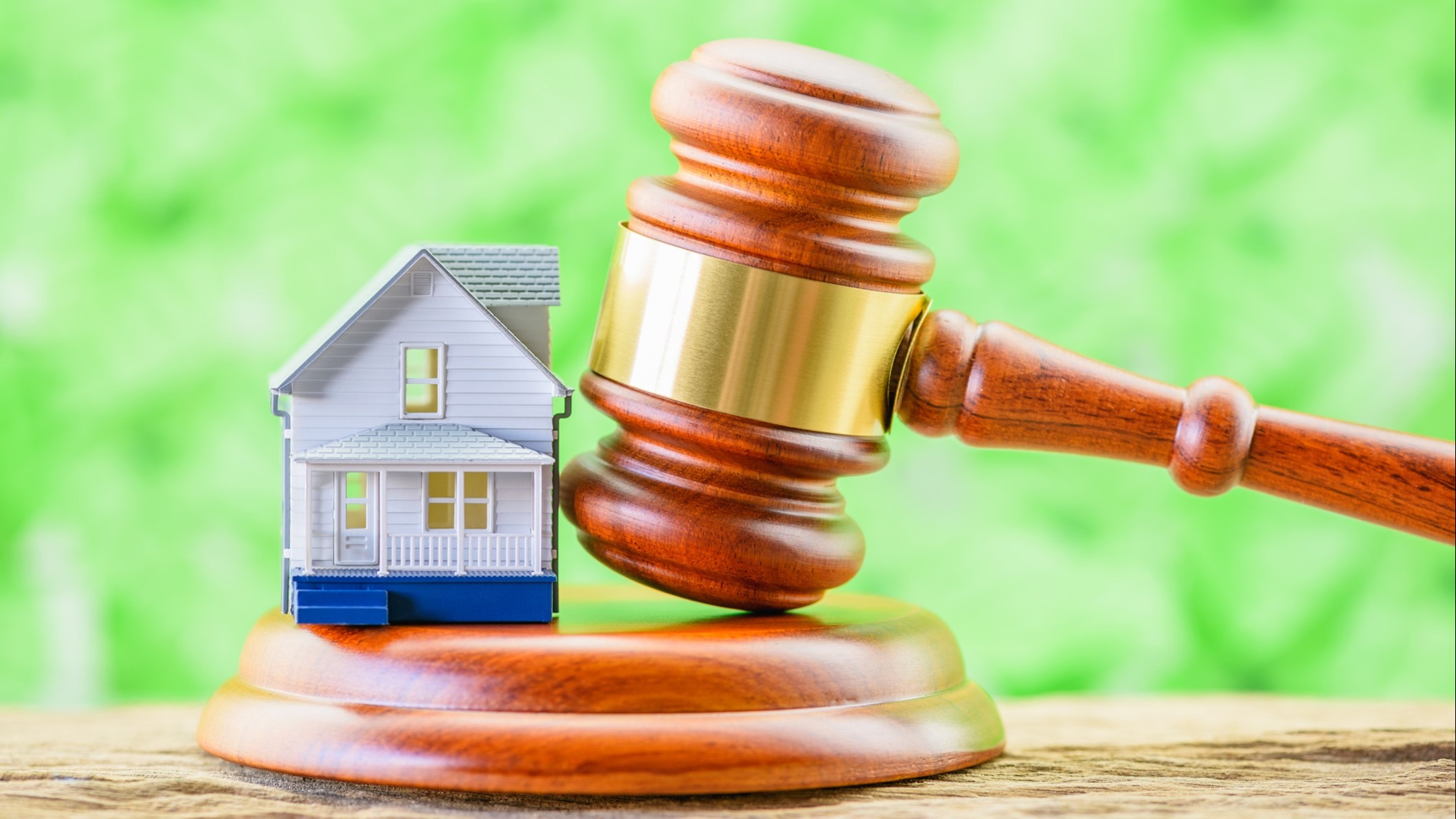 Photo image of a gavel next to a little house with a grass background