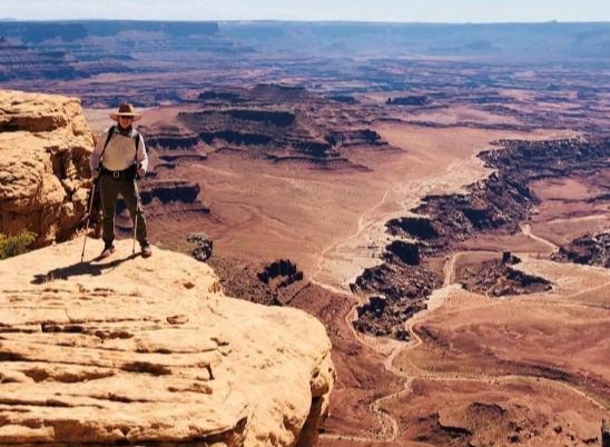 Joseph stands on a cliff, gazing out over a vast canyon, surrounded by rugged rock formations and distant horizons.