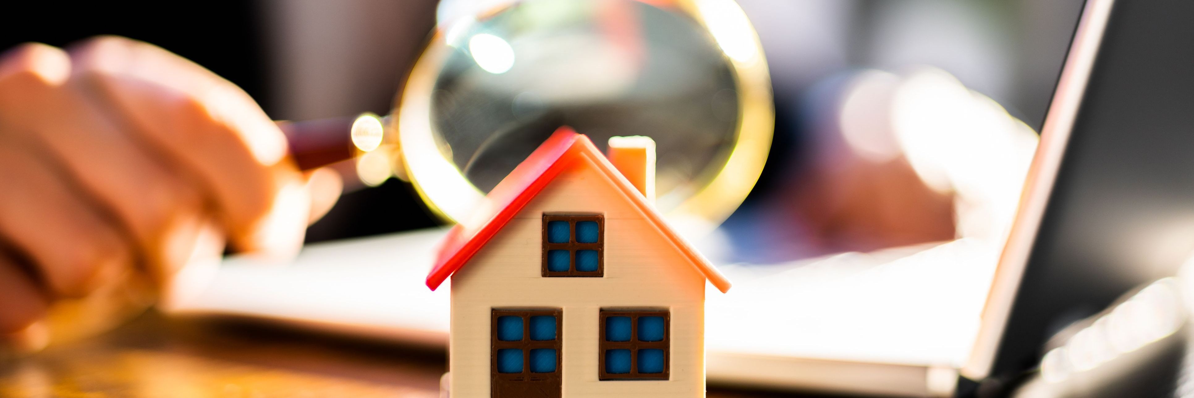 Photo of a person looking through a magnifying glass at a little wooden home