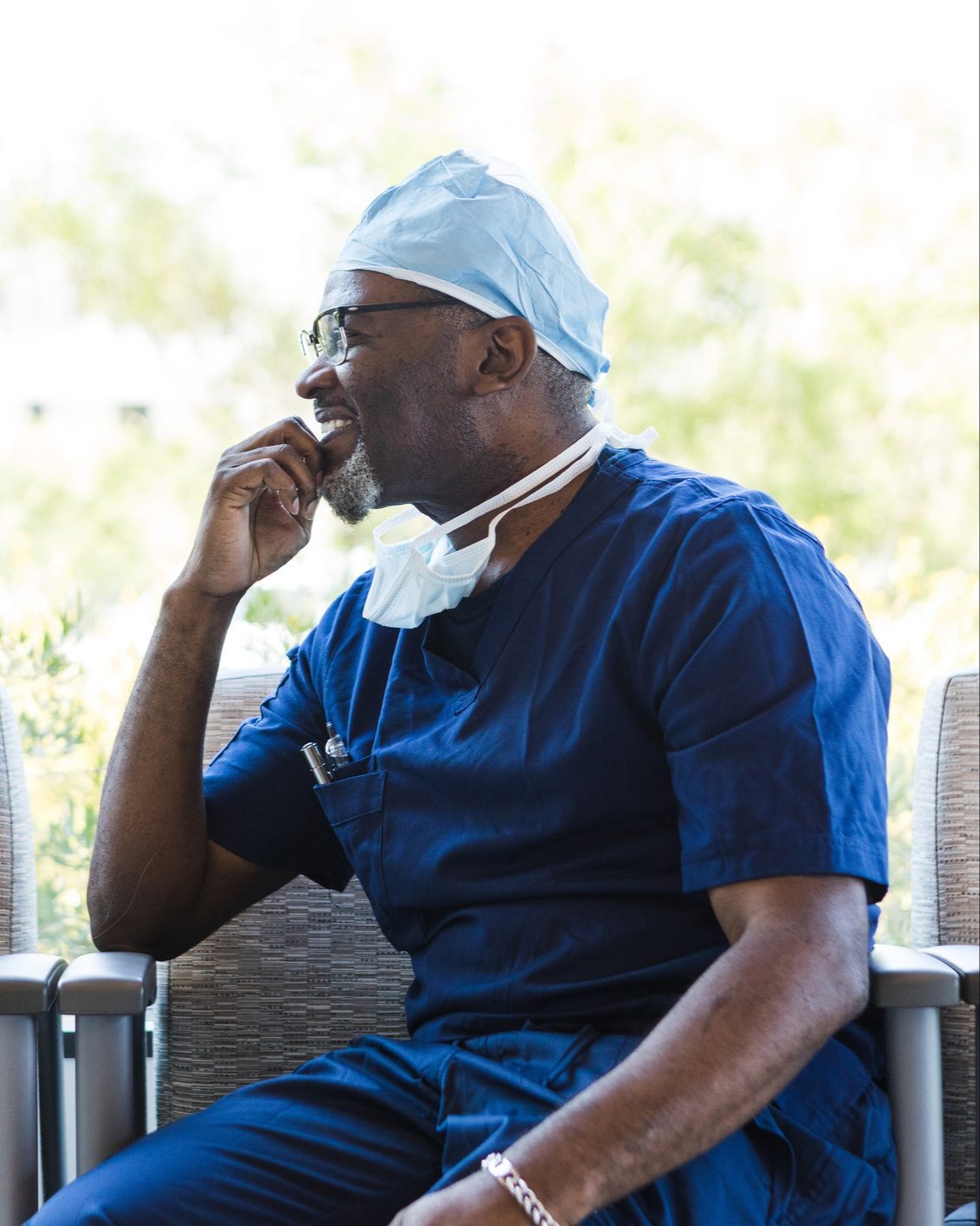 A healthcare professional in scrubs smiling and looking out a sunlit window
