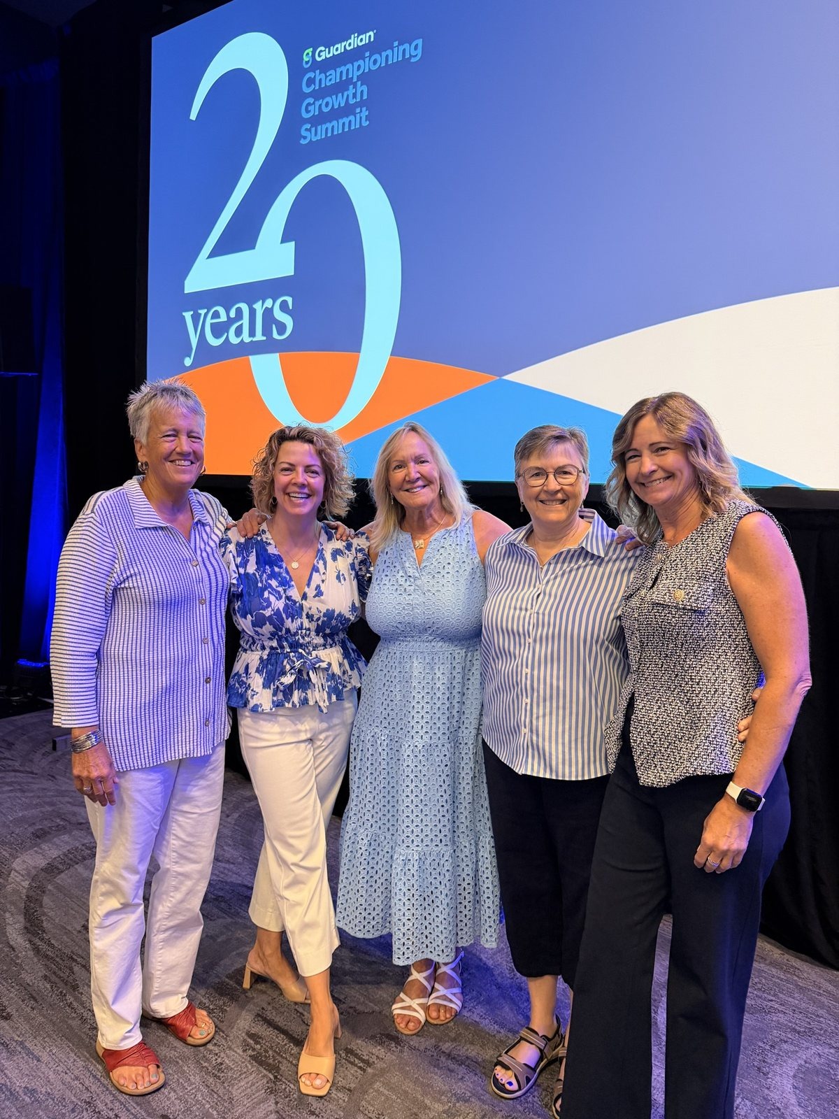 Five women standing arm in arm in front of a Guardian Championing Growth Summit twenty years stage screen