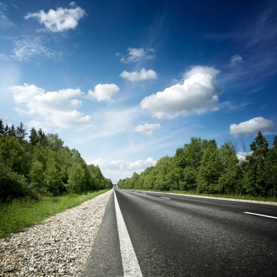 paved road with no cars on it under a blue sky with puffy white clouds