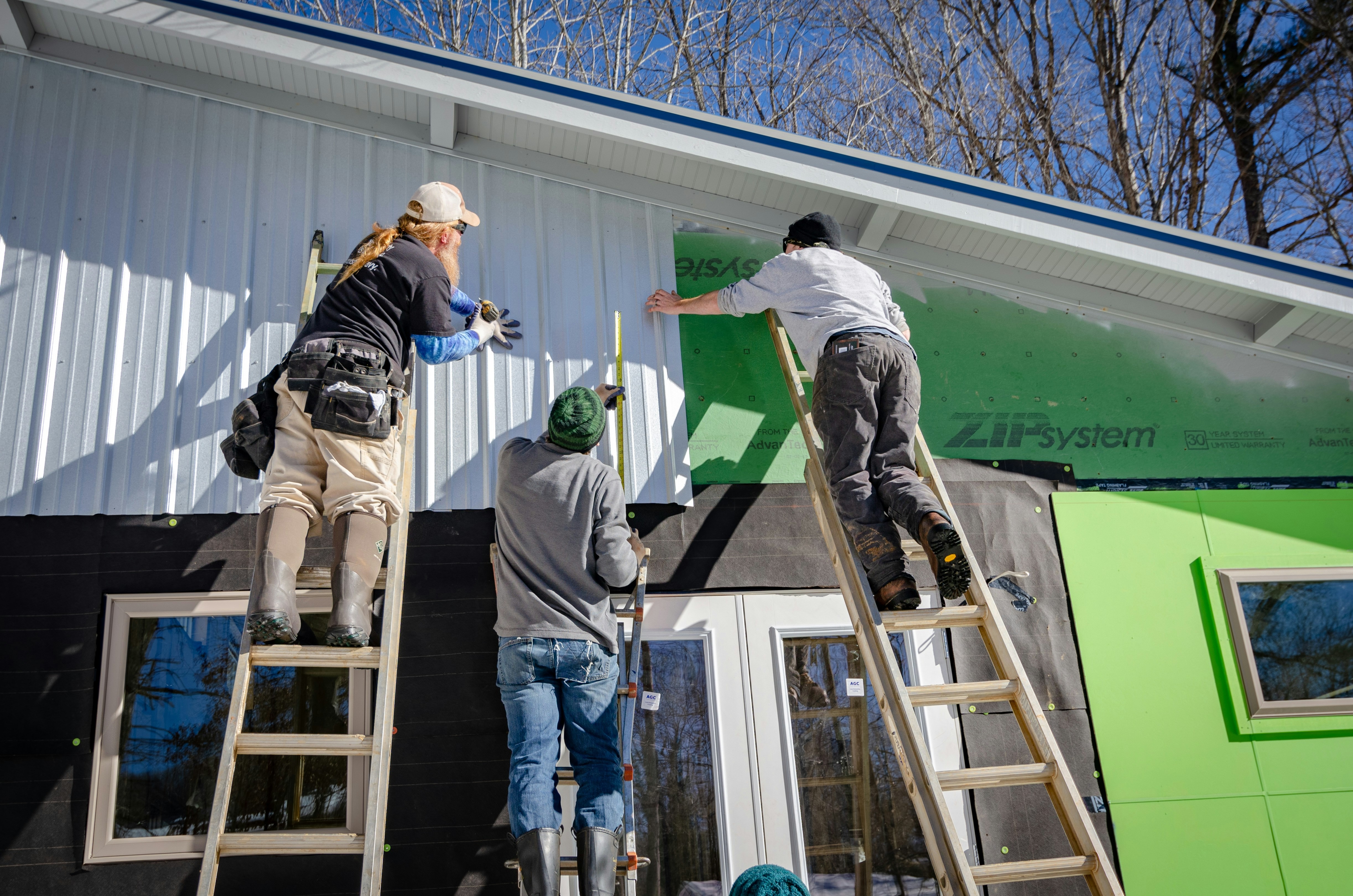 Three people doing renovations on a home; applying paneling to the outside of the house.