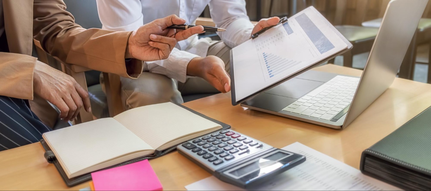 Businesswoman recording financial data and reviewing bookkeeping documents with a calculator and laptop.