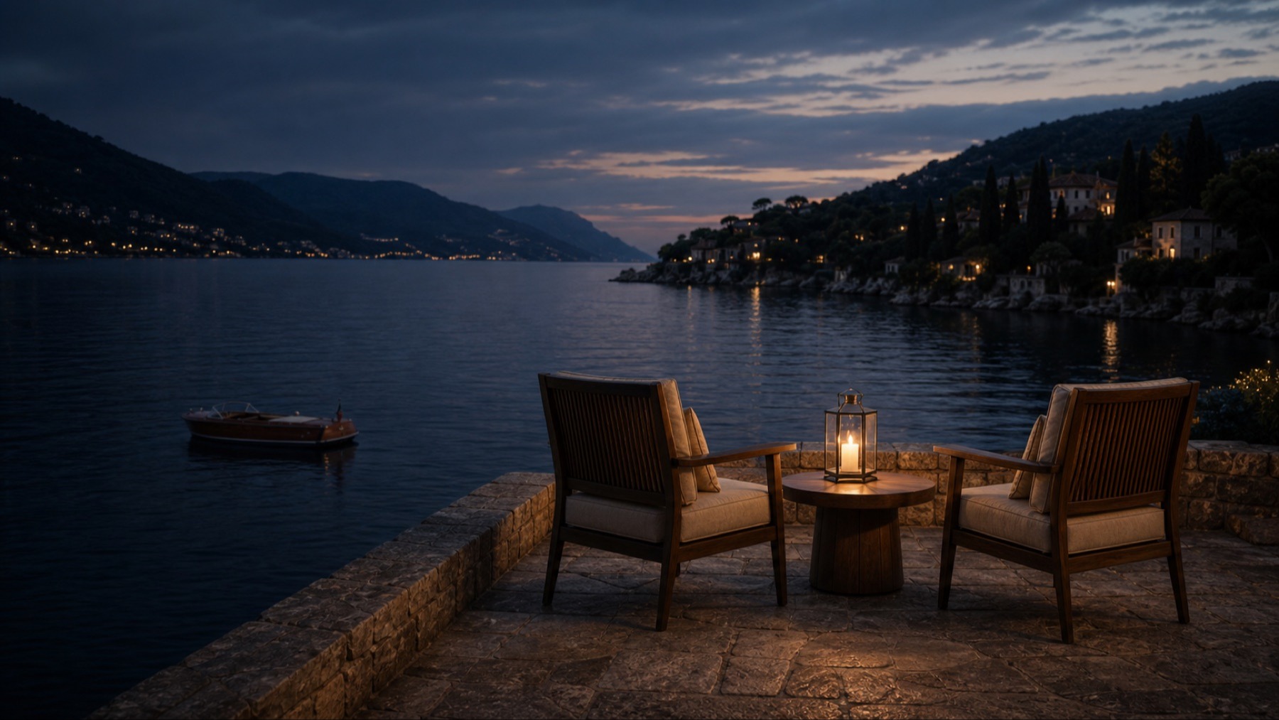 Two wooden chairs and a lantern overlooking a quiet Italian bay at dusk