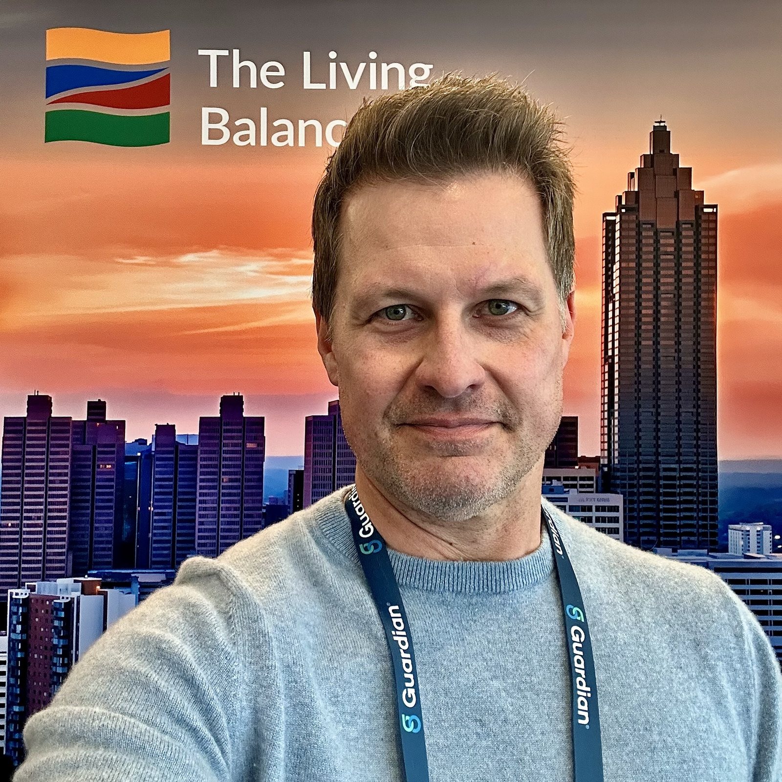 Neill wearing a Guardian lanyard in front of a Living Balance Sheet backdrop with a city skyline