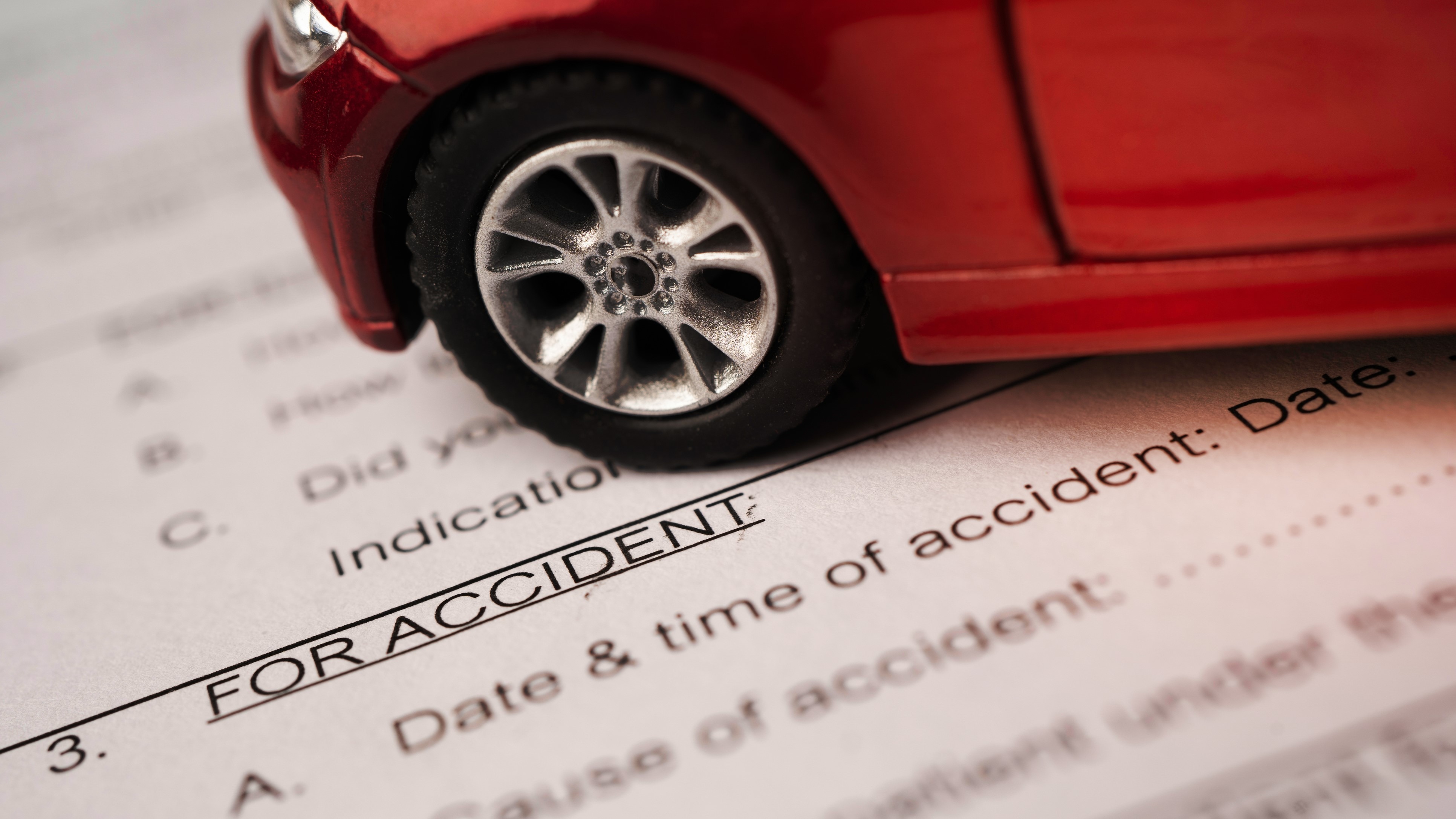 Miniature red sports car sitting on top of an accident form.