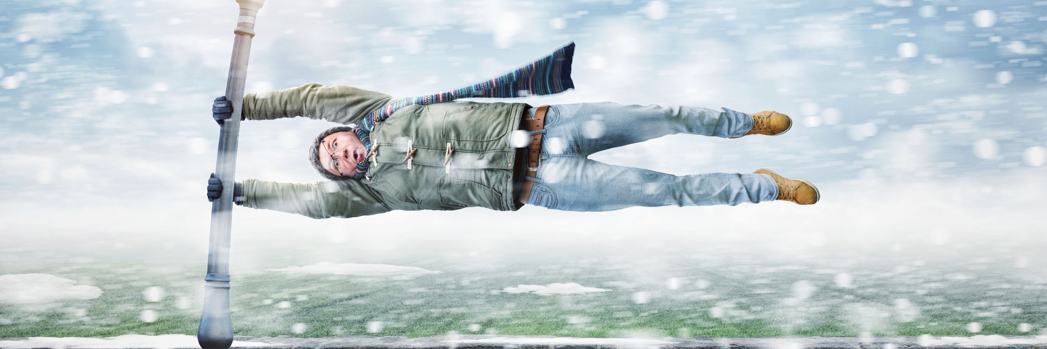 Photo of a man holding onto a pole and being blown horizontally by a windy snow storm.