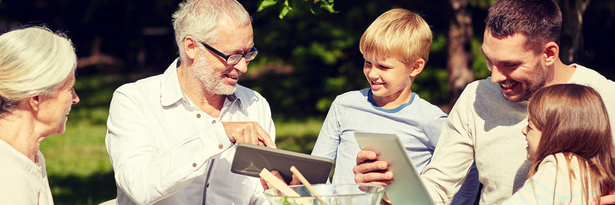 multi-generational family sitting at a picnic table before a meal and looking at tablets