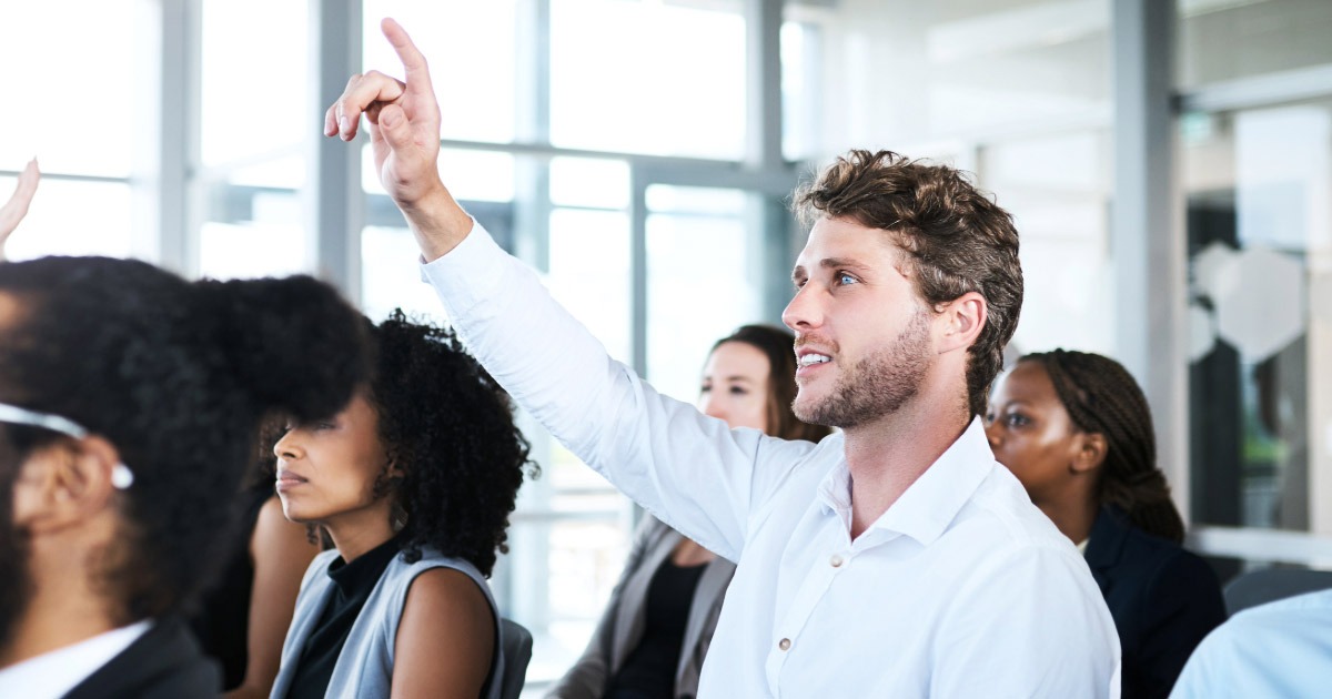 Young man holding his hand up in class to ask a question