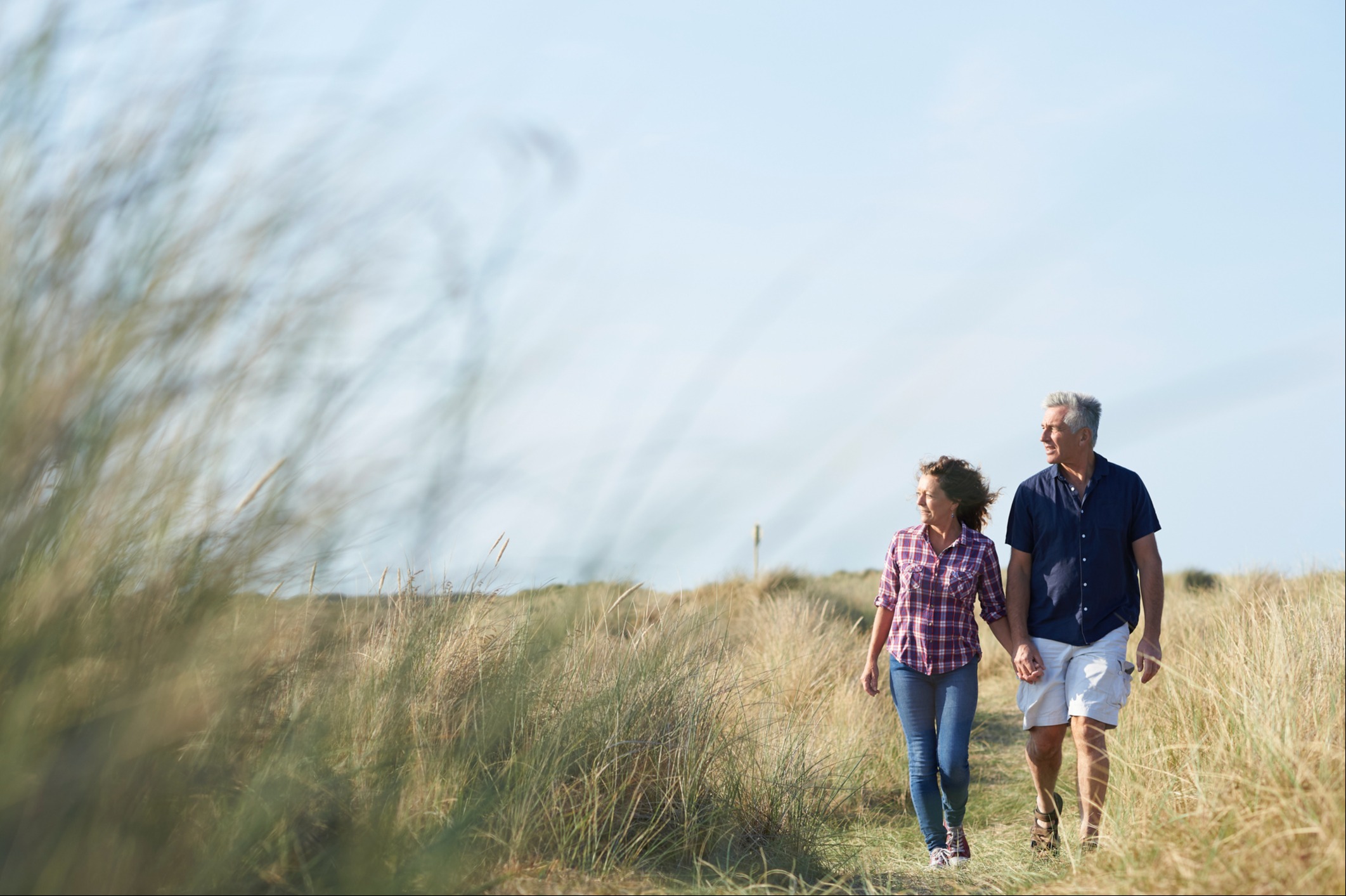 Woman and man holding hands walking through a grass field
