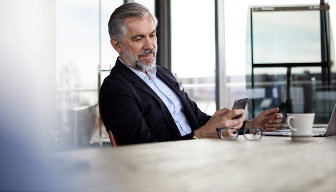 Man drinking coffee and looking at cellphone in a bright office.