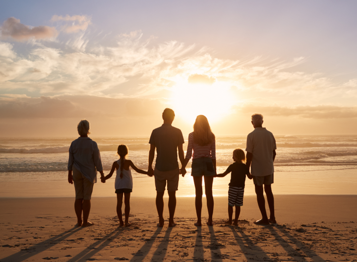 multi-generational family holding hands and watching sunset on the beach