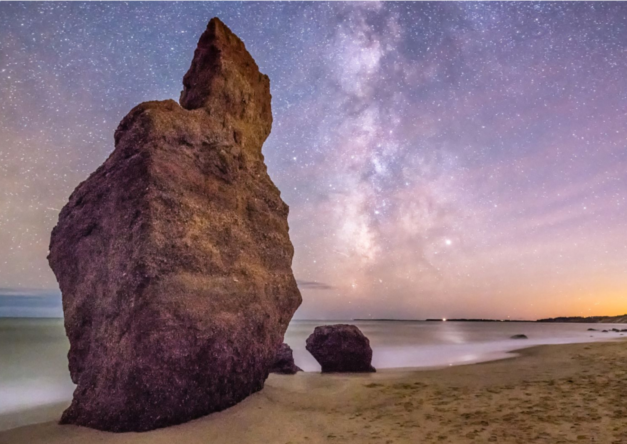 large rocks next to the ocean below the night sky filled with stars