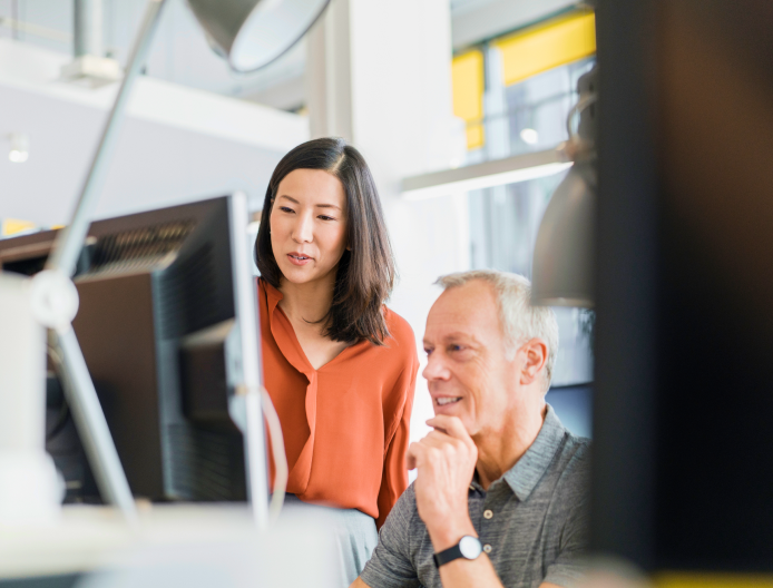 two people working together and looking at a computer monitor