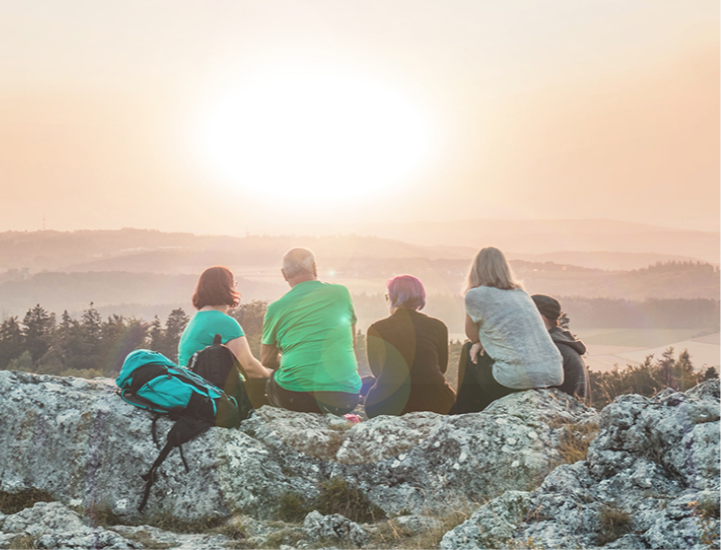Group of older adults sitting on a mountain watching a sunset
