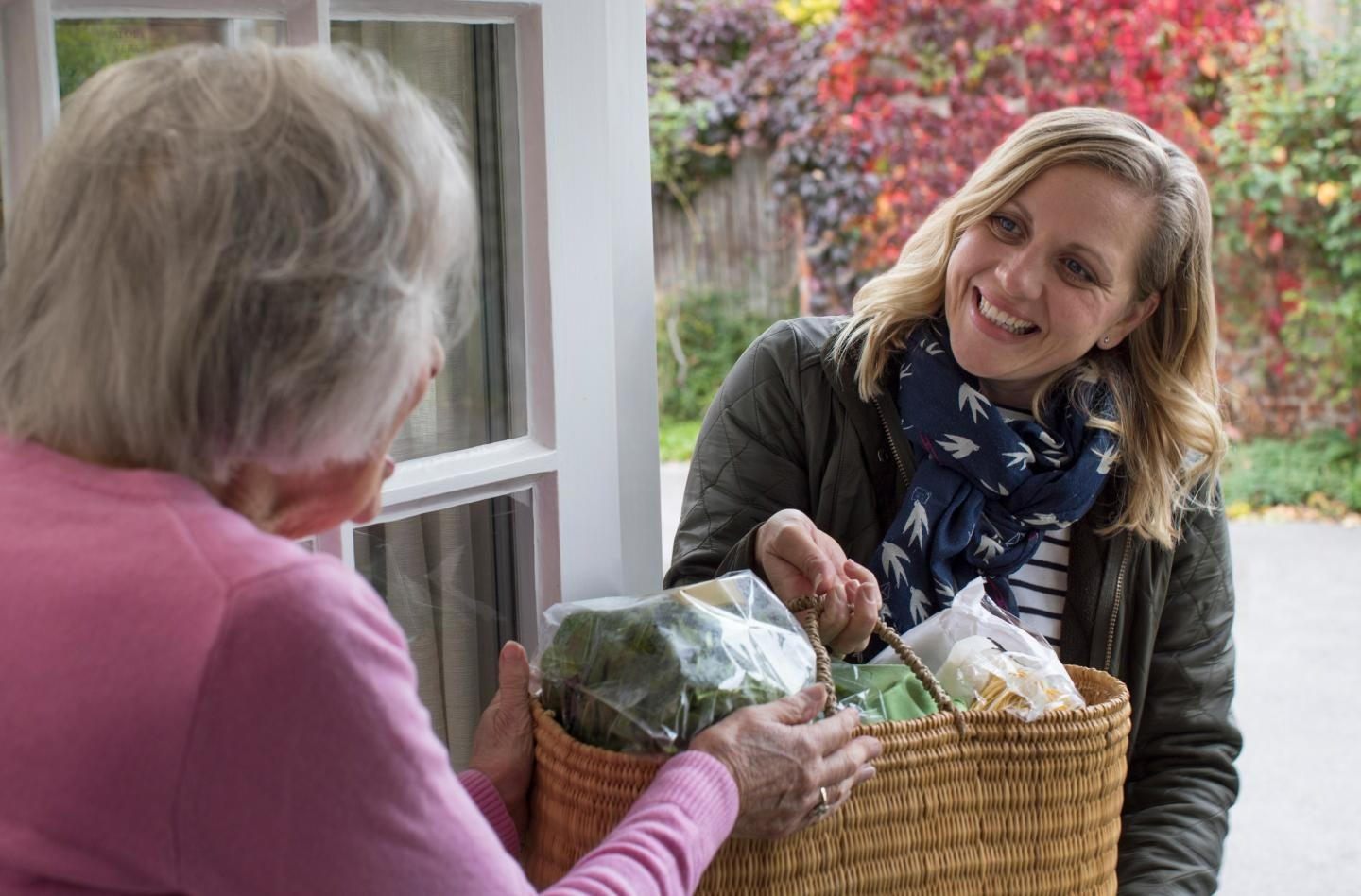 woman handing a basket of groceries to an older woman