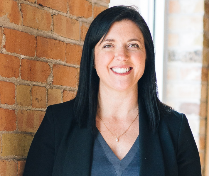 Woman smiling against a brick wall with window behind