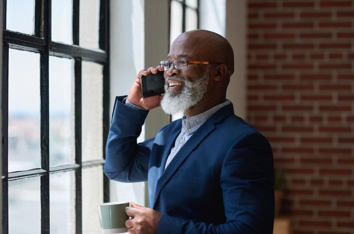 man talking on a cellphone, holding coffee cup and looking out a window