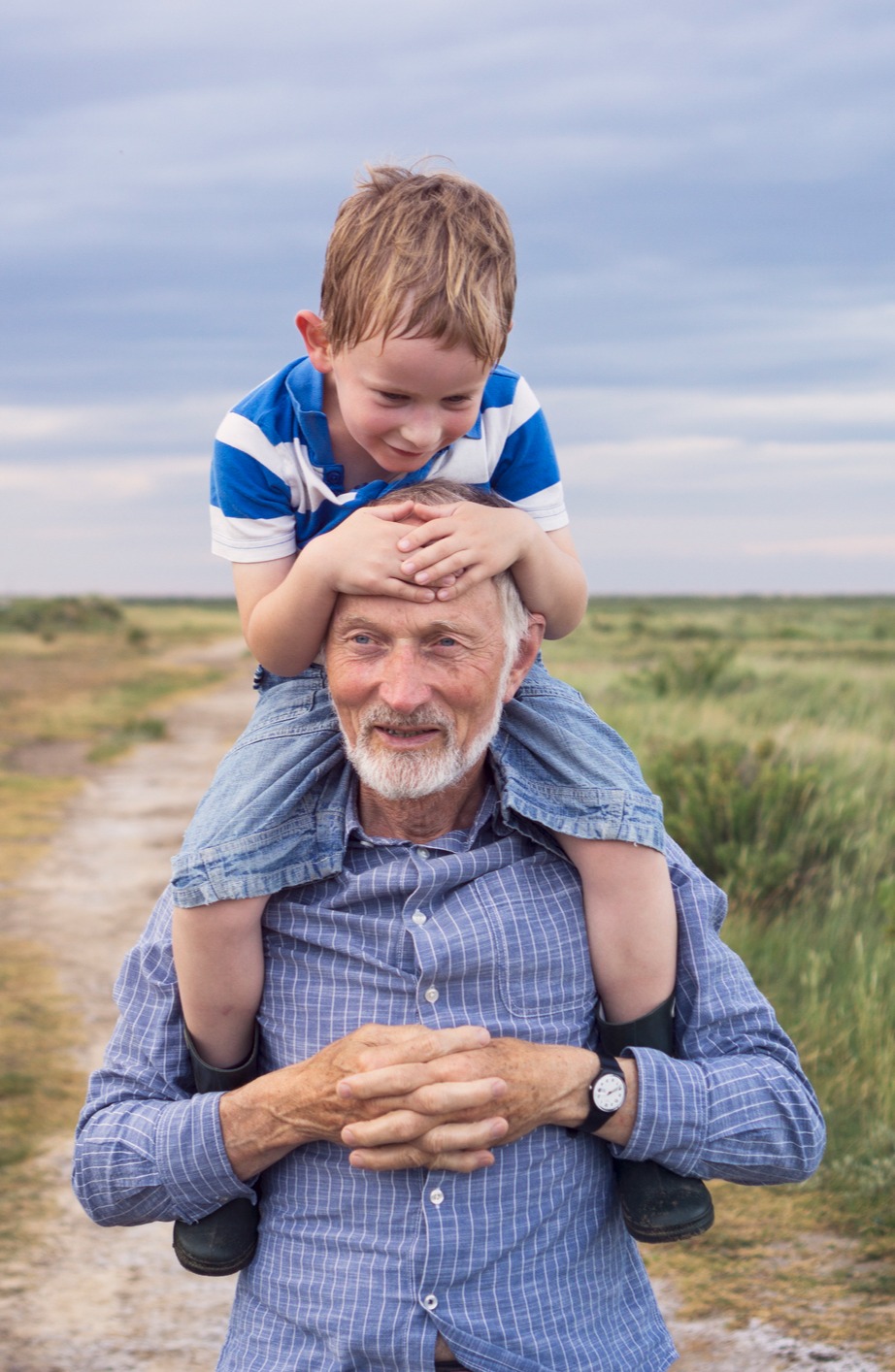 Child-sitting-upon-his-grandfathers-shoulders-on-a-beach-walk