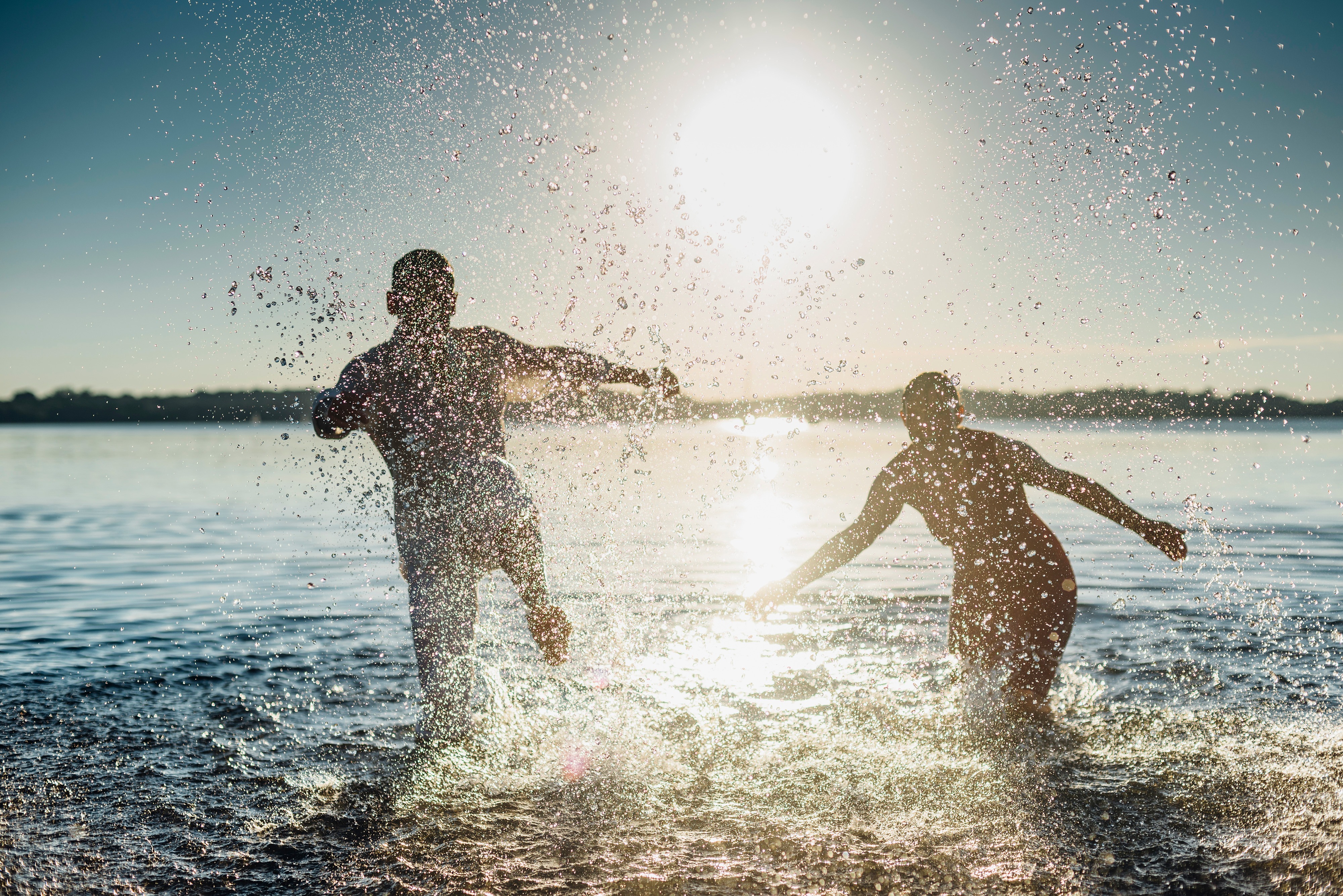 two people splashing in a lake under a big setting sun