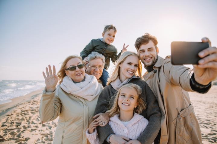 Multi-generational family taking a selfie on a sunny windy beach.